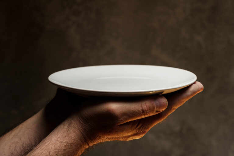 Male hands holding empty plate on dark background, lack of food, hunger concept.